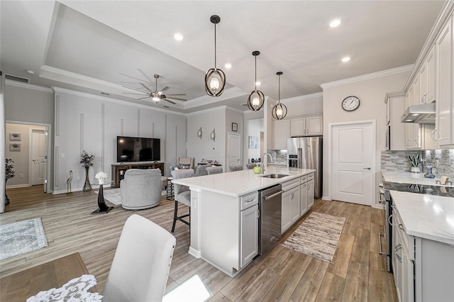 kitchen featuring a kitchen bar, light hardwood / wood-style floors, stainless steel appliances, a center island with sink, and hanging light fixtures