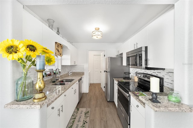 kitchen with tasteful backsplash, stainless steel appliances, sink, white cabinets, and light hardwood / wood-style floors