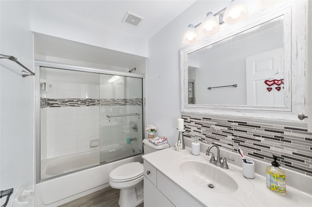 full bathroom with vanity, backsplash, toilet, and bath / shower combo with glass door