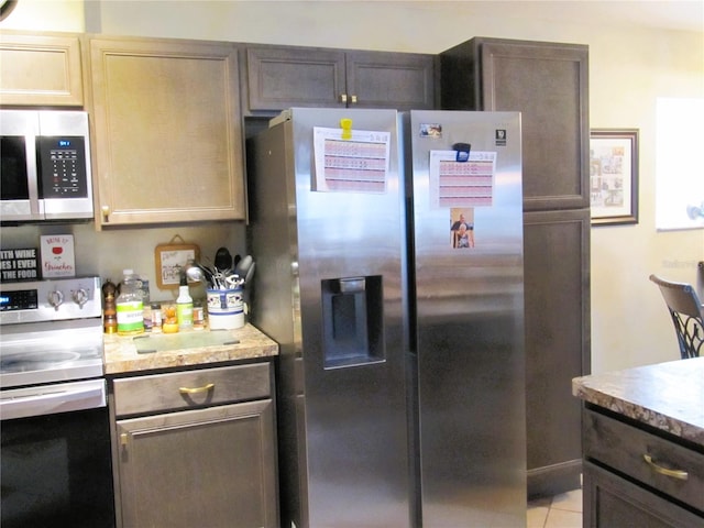 kitchen featuring dark brown cabinetry, appliances with stainless steel finishes, light tile patterned floors, and cream cabinetry