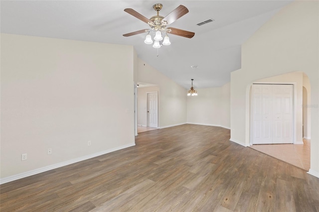 empty room featuring lofted ceiling, dark hardwood / wood-style floors, and ceiling fan with notable chandelier