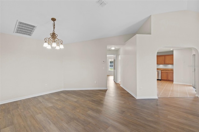 empty room with vaulted ceiling, light hardwood / wood-style floors, and a notable chandelier