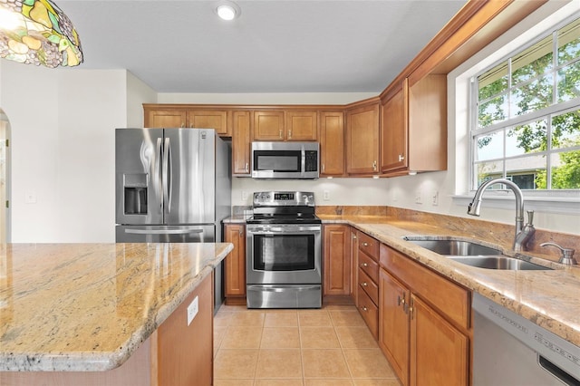 kitchen with appliances with stainless steel finishes, sink, light tile patterned floors, and light stone counters