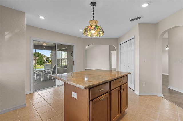 kitchen featuring light tile patterned flooring, light stone countertops, a center island, and pendant lighting