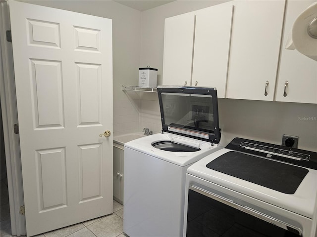 clothes washing area featuring light tile patterned floors, cabinets, and washer and clothes dryer