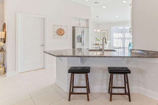 kitchen with stainless steel fridge with ice dispenser, a kitchen breakfast bar, sink, pendant lighting, and dark stone counters