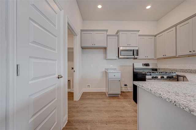 kitchen featuring gray cabinetry, light stone countertops, light wood-type flooring, and appliances with stainless steel finishes