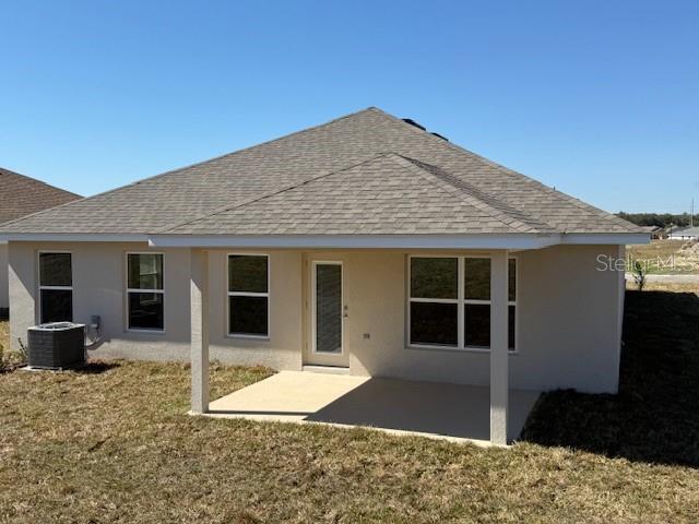3127 NE 45th Ave, Ocala, FL 34470 - rear view of house featuring stucco siding, a lawn, a patio area, a shingled roof, and central AC unit
