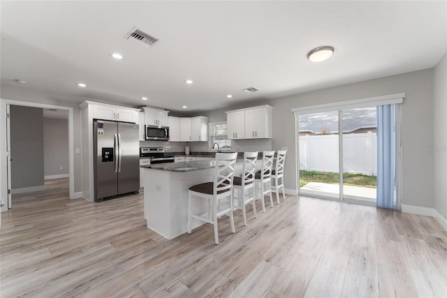 kitchen with a kitchen breakfast bar, white cabinetry, dark stone counters, light hardwood / wood-style flooring, and stainless steel appliances