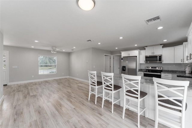 kitchen featuring decorative backsplash, a kitchen breakfast bar, white cabinetry, appliances with stainless steel finishes, and light hardwood / wood-style floors