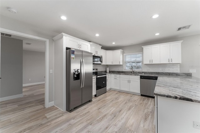 kitchen featuring backsplash, stainless steel appliances, white cabinets, dark stone countertops, and light hardwood / wood-style flooring