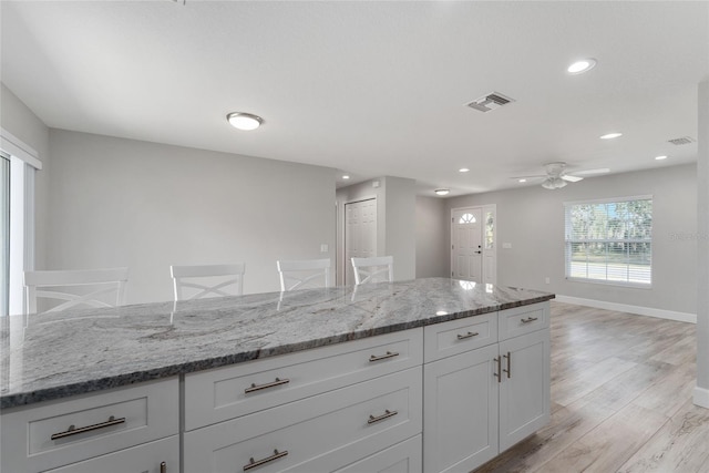 kitchen with a kitchen breakfast bar, white cabinets, light stone counters, and light wood-type flooring