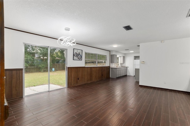 unfurnished living room featuring a textured ceiling, dark hardwood / wood-style floors, an inviting chandelier, and wood walls