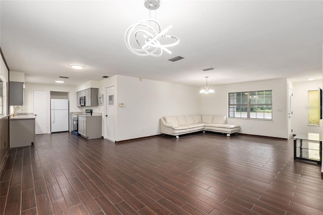 unfurnished living room featuring a notable chandelier, sink, and dark hardwood / wood-style floors