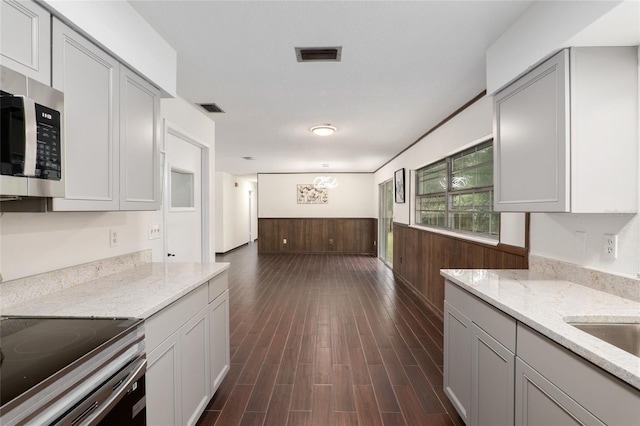 kitchen with light stone countertops, stainless steel appliances, dark wood-type flooring, and gray cabinetry