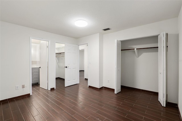 unfurnished bedroom with a textured ceiling, ensuite bathroom, and dark hardwood / wood-style floors