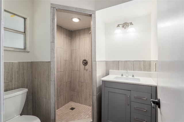 bathroom featuring vanity, toilet, tile walls, and a tile shower