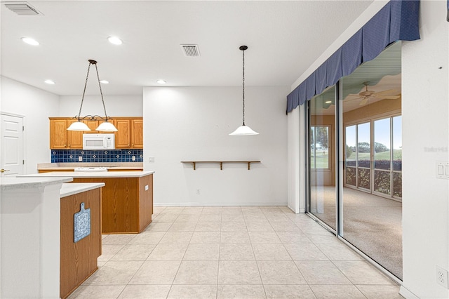 kitchen featuring white microwave, visible vents, light countertops, a center island, and brown cabinetry