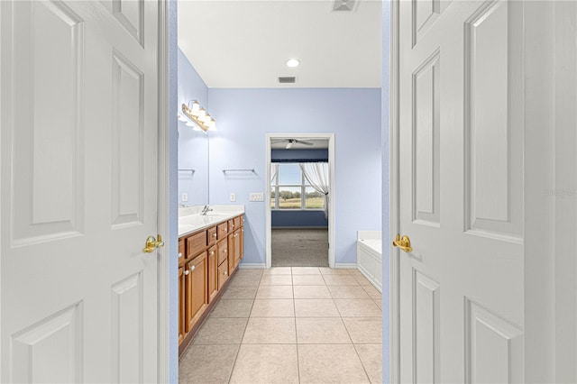 bathroom with tile patterned flooring, visible vents, baseboards, a bath, and double vanity