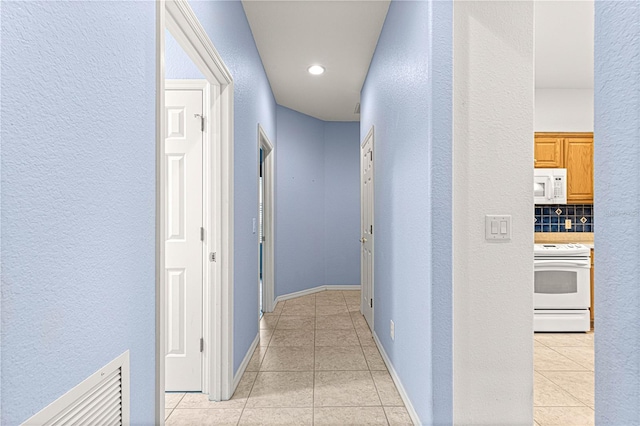 hall with a textured wall, baseboards, and light tile patterned floors