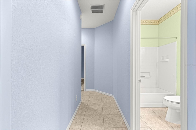 corridor featuring light tile patterned floors, baseboards, visible vents, and a textured wall