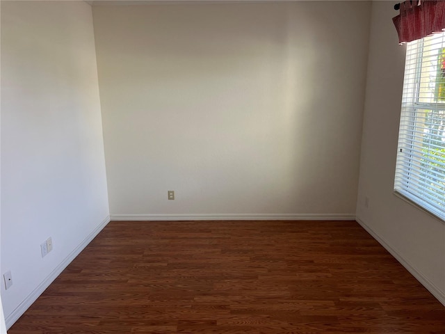 empty room featuring baseboards and dark wood-type flooring