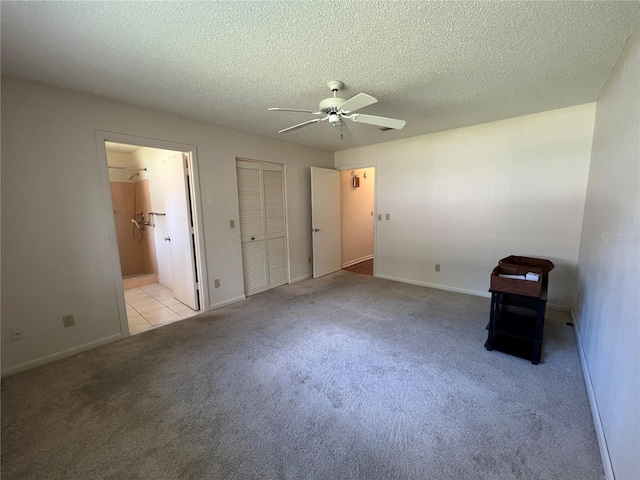 unfurnished bedroom featuring ceiling fan, light carpet, a textured ceiling, and ensuite bath