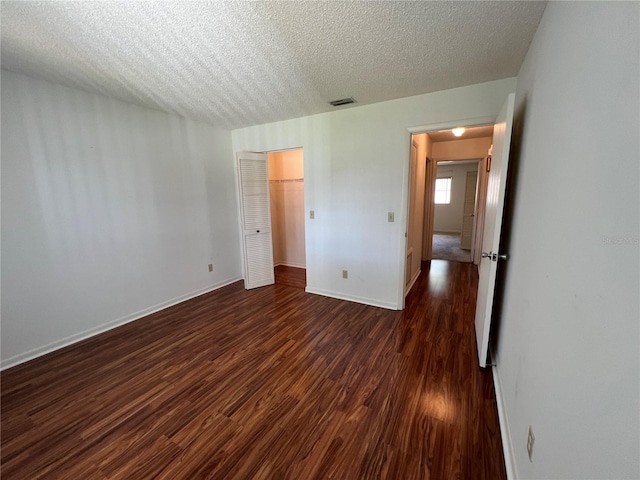 unfurnished bedroom with a textured ceiling, dark hardwood / wood-style floors, and a closet