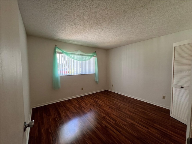 empty room with a textured ceiling and dark hardwood / wood-style flooring