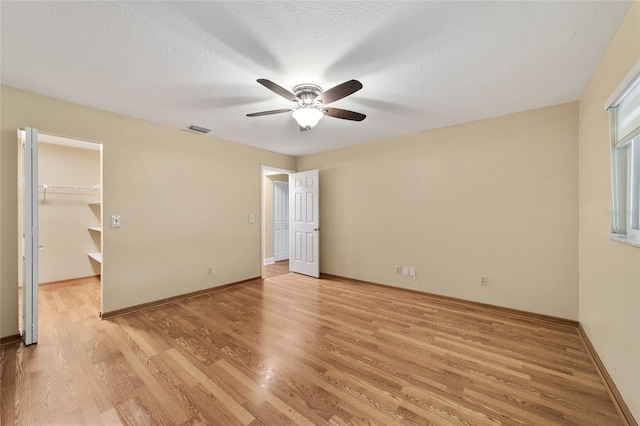 unfurnished bedroom featuring a closet, a spacious closet, light wood-type flooring, a textured ceiling, and ceiling fan