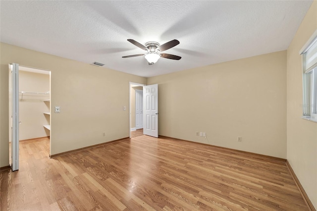 unfurnished bedroom with ceiling fan, a walk in closet, a textured ceiling, and light hardwood / wood-style flooring