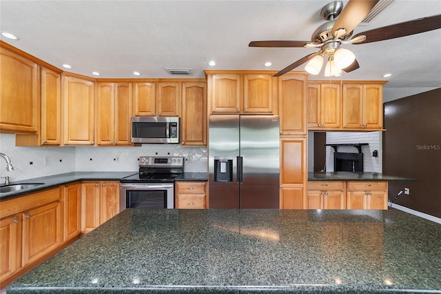 kitchen featuring decorative backsplash, ceiling fan, appliances with stainless steel finishes, dark stone countertops, and sink