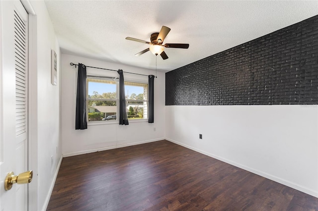 empty room featuring ceiling fan, brick wall, a textured ceiling, and dark hardwood / wood-style floors