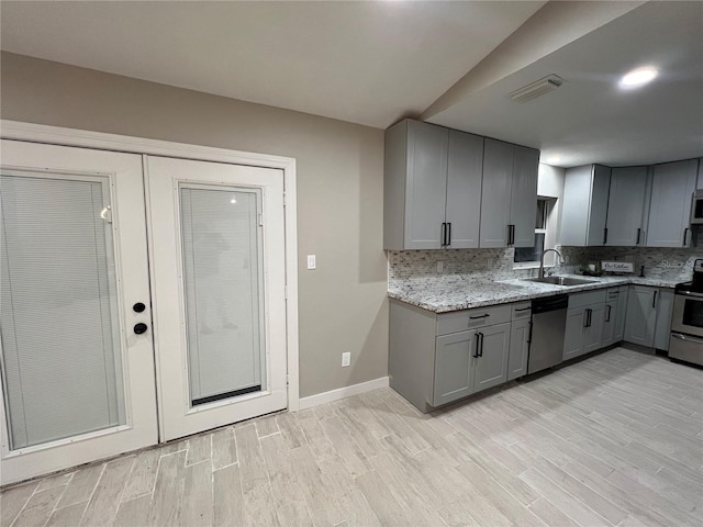 kitchen with stainless steel appliances, sink, light stone counters, decorative backsplash, and gray cabinets