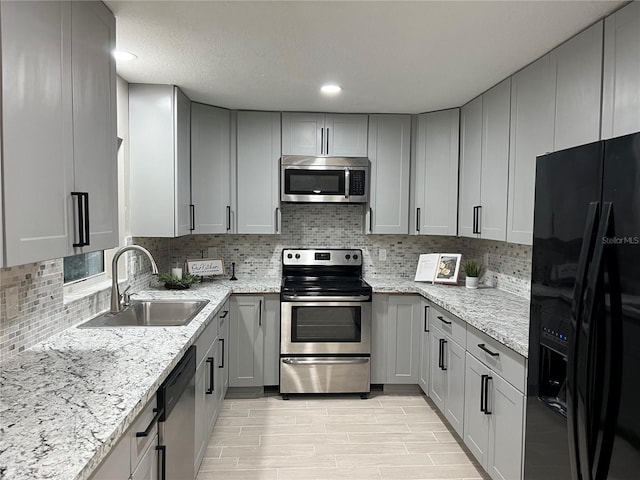 kitchen featuring appliances with stainless steel finishes, light stone countertops, gray cabinets, and sink