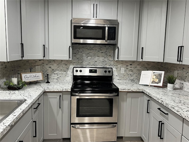 kitchen featuring light stone countertops, appliances with stainless steel finishes, backsplash, and gray cabinetry