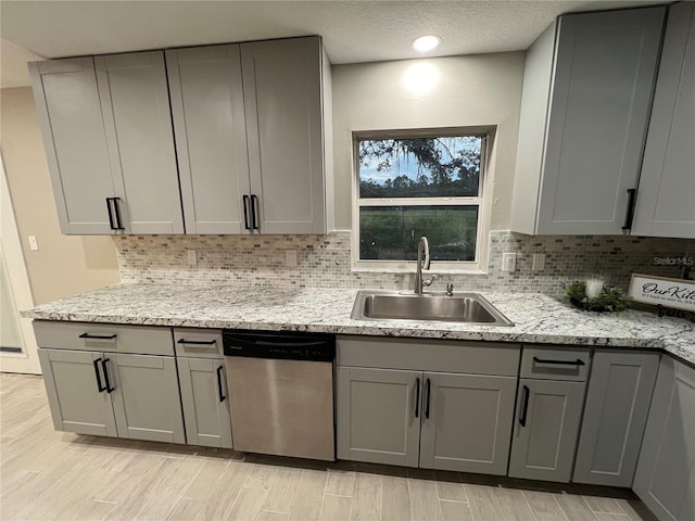 kitchen featuring sink, dishwasher, gray cabinetry, and light stone countertops