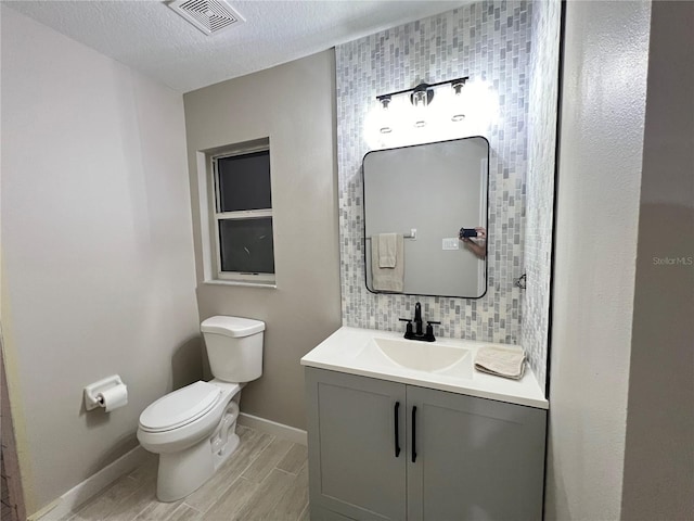 bathroom with a textured ceiling, vanity, decorative backsplash, and toilet