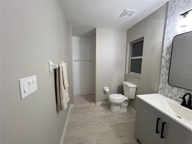 bathroom featuring toilet, vanity, a tile shower, decorative backsplash, and a textured ceiling