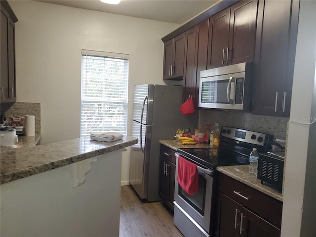 kitchen featuring light hardwood / wood-style floors, light stone counters, dark brown cabinetry, and appliances with stainless steel finishes