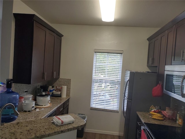 kitchen with black stove, light stone counters, dark brown cabinetry, hardwood / wood-style floors, and fridge