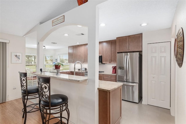 kitchen featuring a center island with sink, light stone counters, a breakfast bar area, light wood-type flooring, and stainless steel fridge