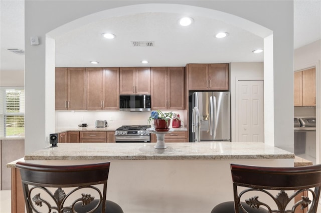 kitchen with appliances with stainless steel finishes, washing machine and dryer, a breakfast bar, and light stone countertops