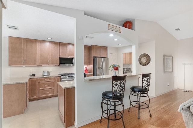 kitchen featuring stainless steel appliances, lofted ceiling, light hardwood / wood-style floors, light stone counters, and a breakfast bar area