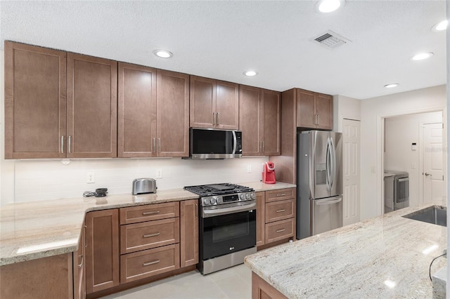 kitchen with stainless steel appliances, light stone counters, tasteful backsplash, light tile patterned floors, and washer and dryer