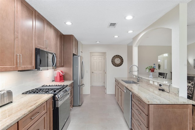 kitchen featuring backsplash, appliances with stainless steel finishes, light stone countertops, sink, and kitchen peninsula