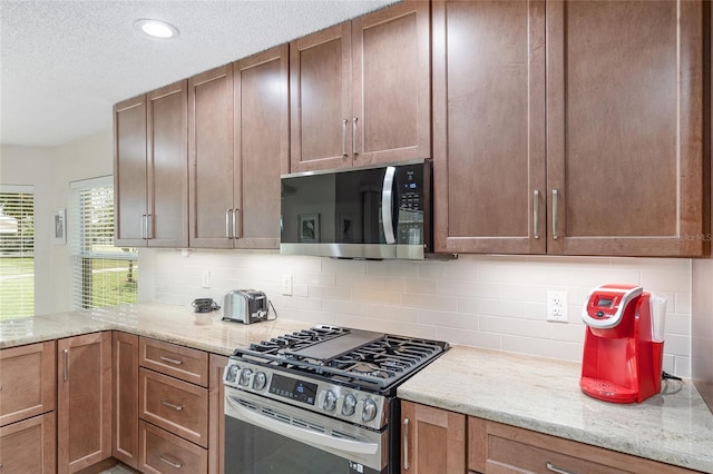 kitchen featuring backsplash, a textured ceiling, light stone countertops, and stainless steel appliances