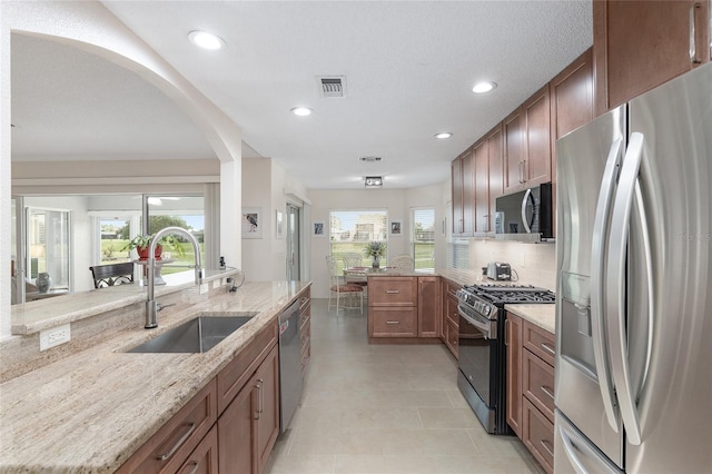 kitchen with tasteful backsplash, light stone counters, appliances with stainless steel finishes, sink, and kitchen peninsula