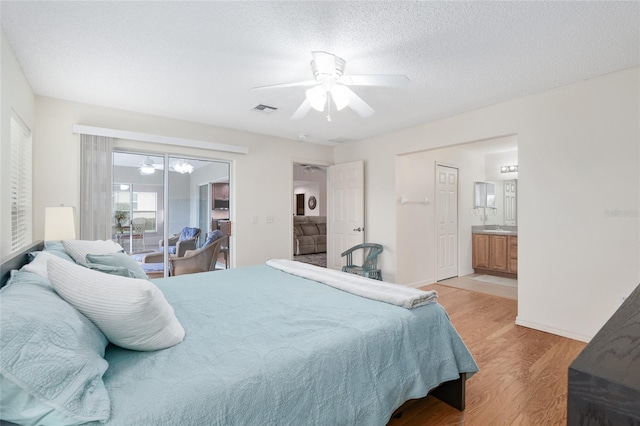 bedroom featuring light hardwood / wood-style floors, ceiling fan, connected bathroom, and a textured ceiling