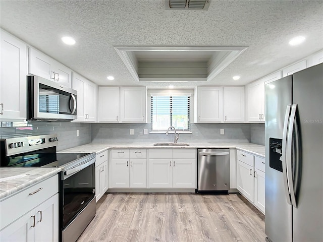 kitchen with stainless steel appliances, a raised ceiling, white cabinetry, and sink